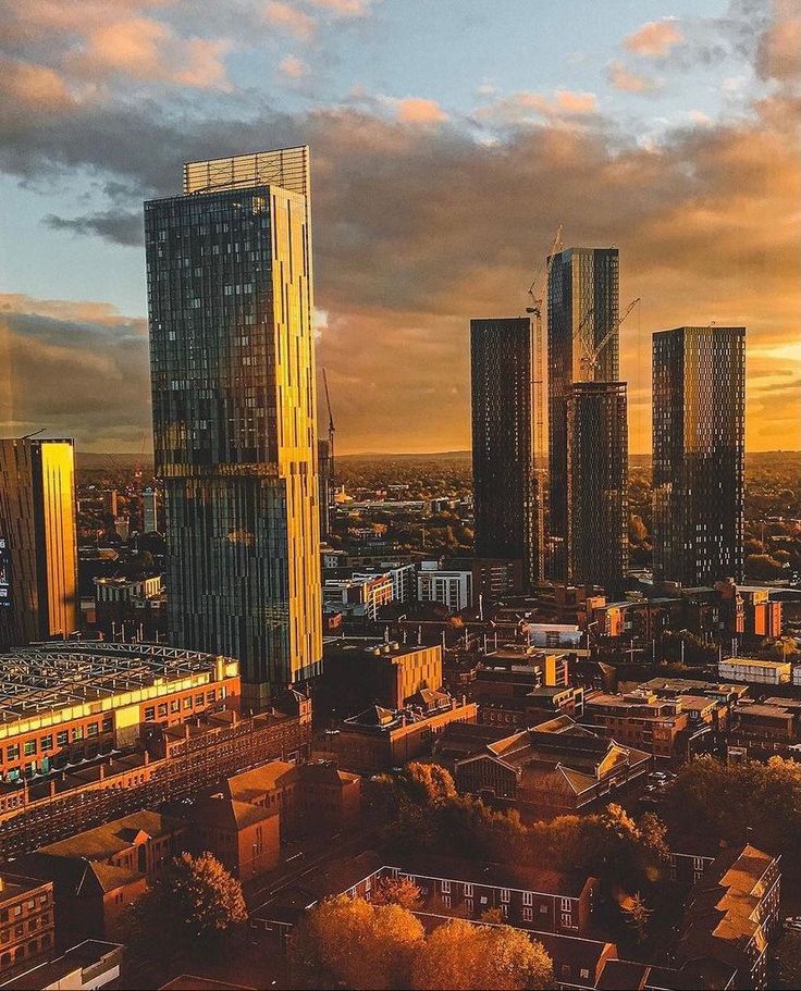 an aerial view of a city with tall buildings and clouds in the background at sunset