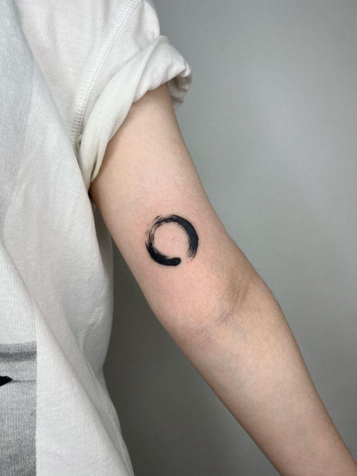 a woman's arm with a black circle tattoo on the left side of her arm