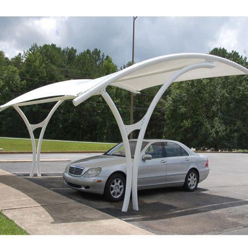 a silver car parked under a white canopy in a parking lot next to some trees