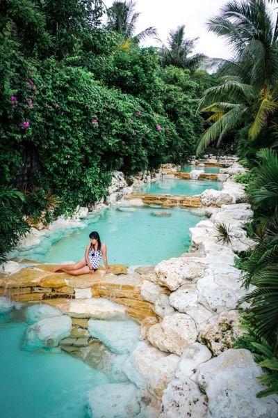 a woman is sitting on the edge of a pool surrounded by rocks and palm trees