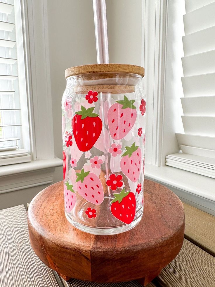 a glass jar with strawberries on it sitting on top of a wooden table next to a window