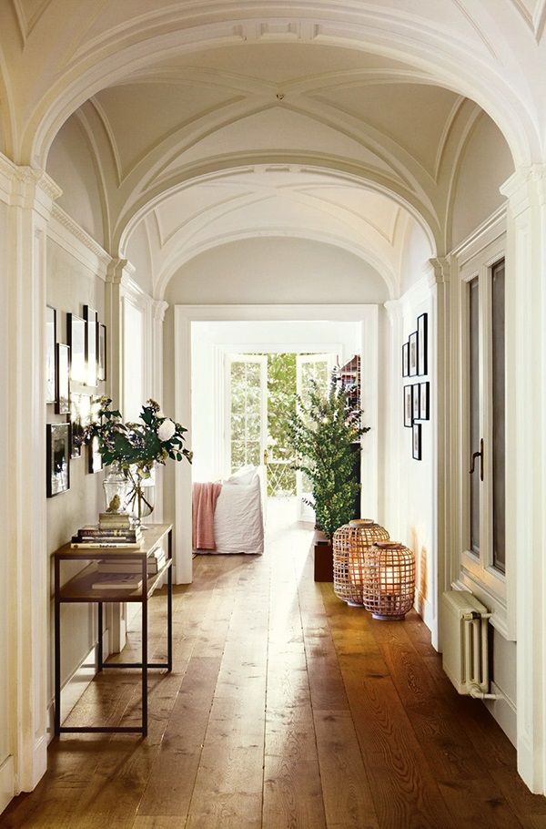 a hallway with wooden floors and white walls, along with potted plants on the far wall