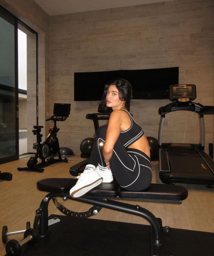 a woman sitting on top of a bench in front of a gym equipment set up