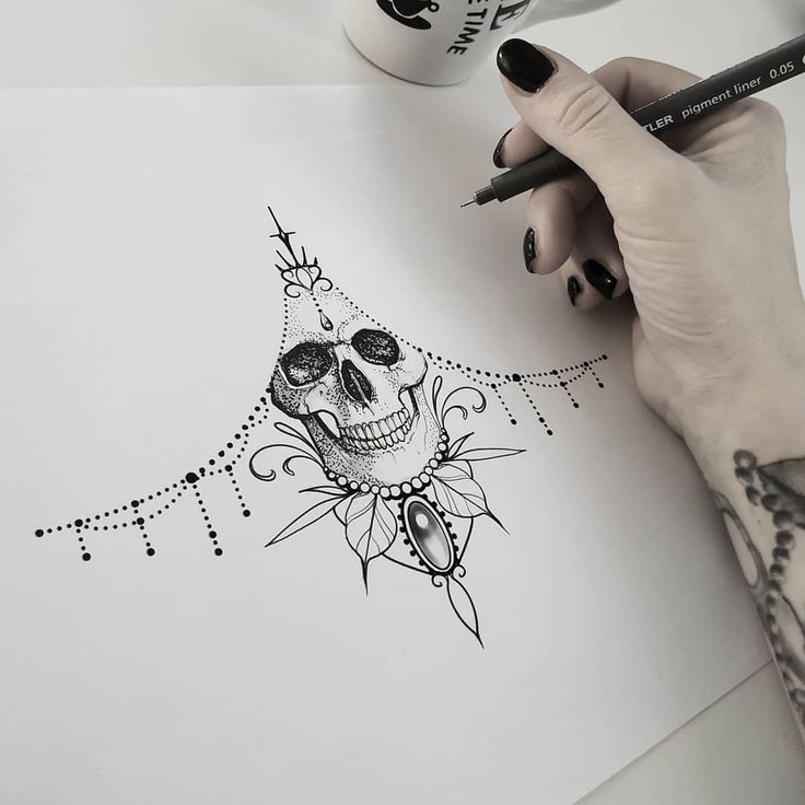 a woman's hand holding a pencil and drawing a skull with flowers on it