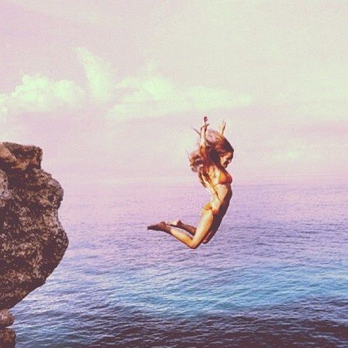 a woman jumping off rocks into the ocean