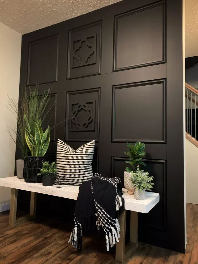 a bench with some plants on top of it next to a black paneled wall