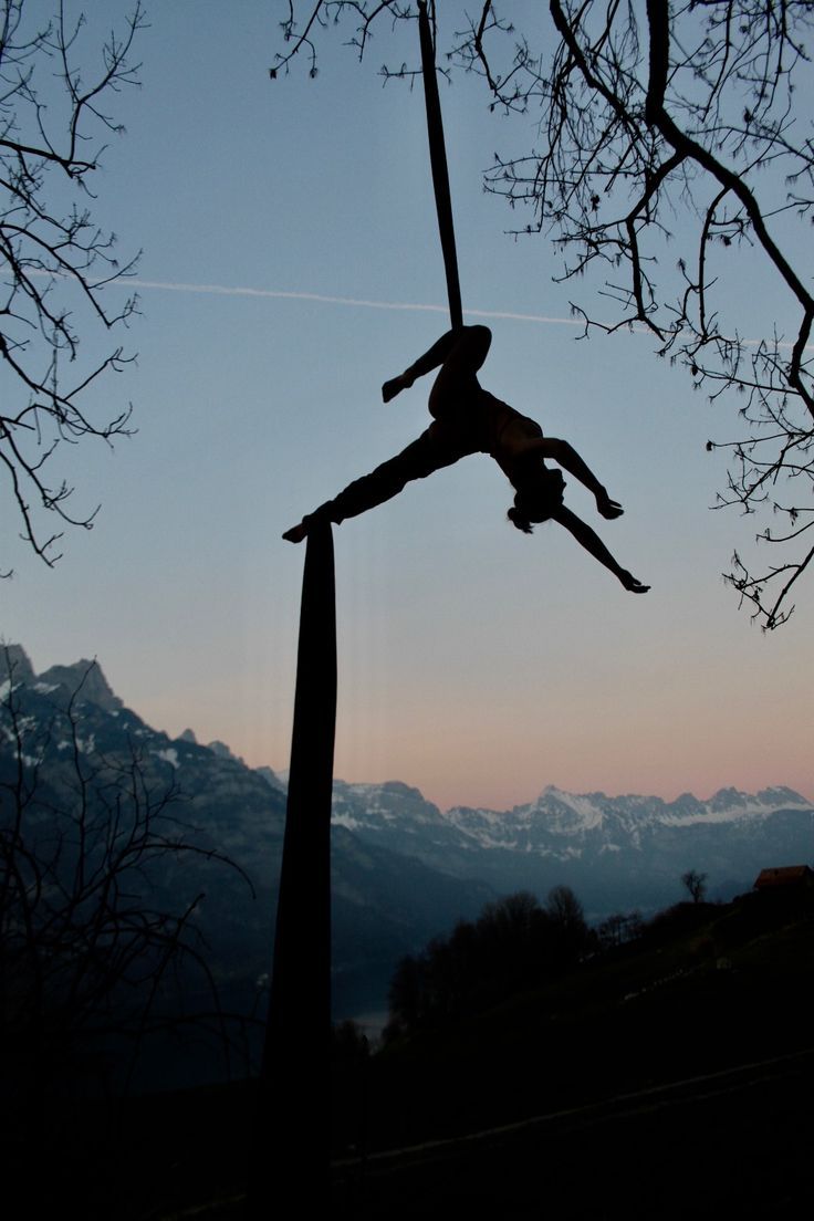 a person is performing aerial acrobatics on a pole in front of mountains