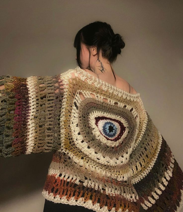 a woman wearing a crocheted sweater with an eye on it's back