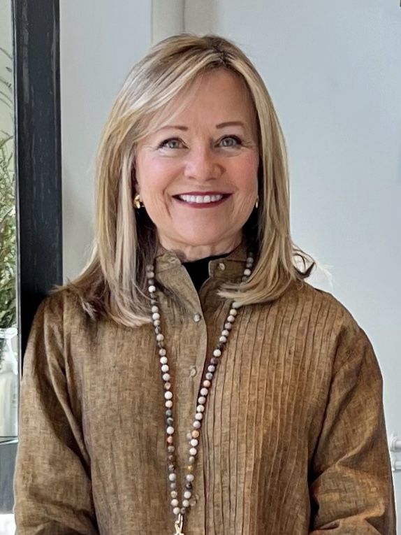 a woman standing in front of a window wearing a brown shirt and beaded necklace