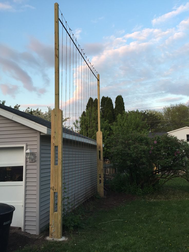 a wooden fence next to a garage in the evening sun with clouds above it and a black trash can nearby