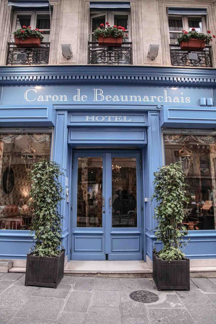 a blue building with potted plants in front of the door and windows that say caron de beaumarchais