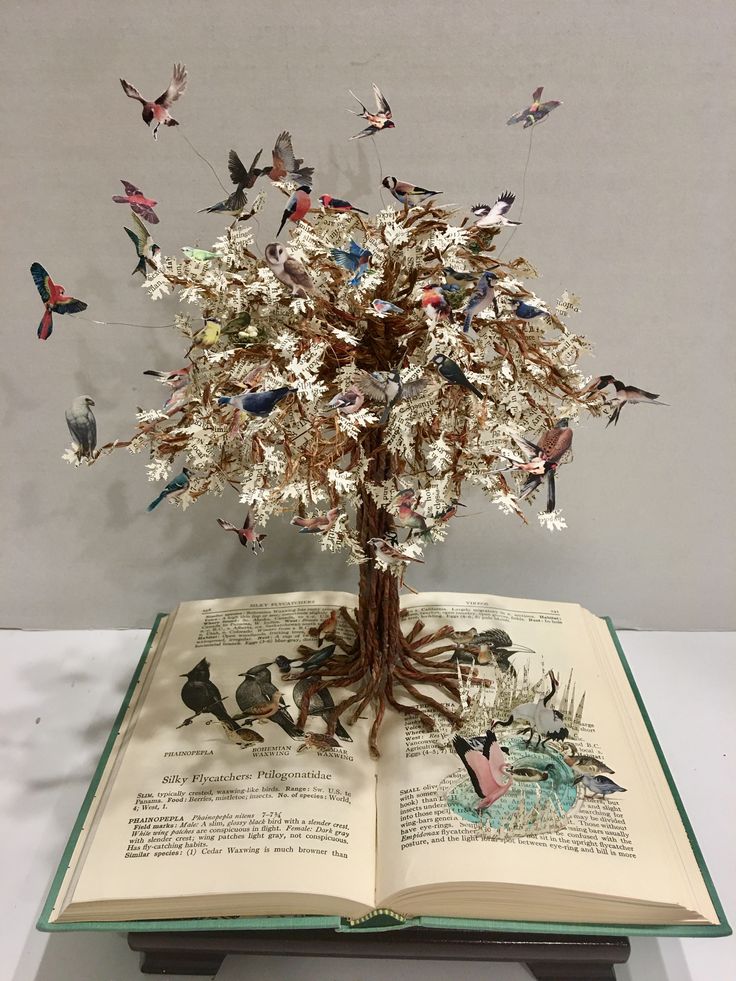 an open book with birds flying around it and on top of the pages is a tree made out of books