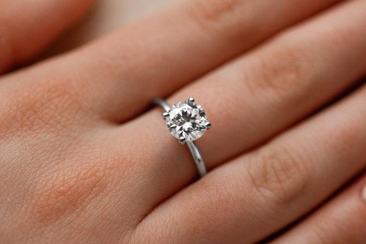 a woman's hand with a diamond ring on top of her finger, showing the center stone