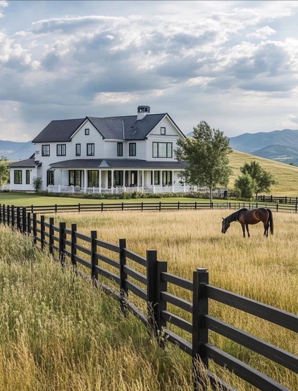 a horse grazes in front of a large white house on a hill with mountains in the background