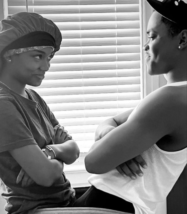 two young women sitting next to each other in front of a window with blinds on the windowsill