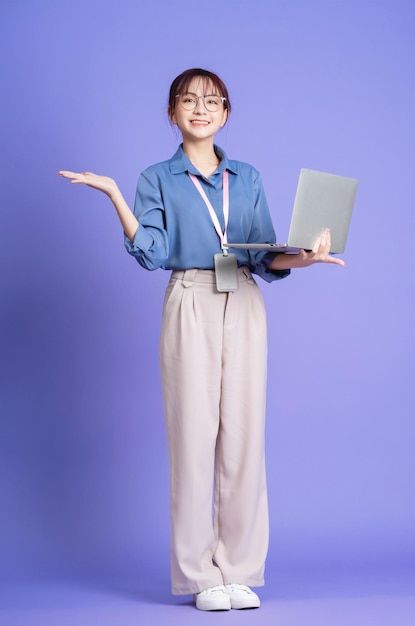 a woman holding a laptop computer on her left hand while standing in front of a purple background