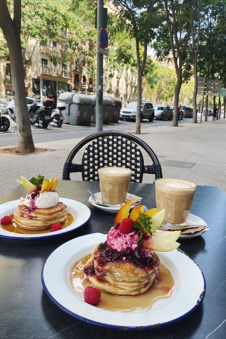 two plates with pancakes and fruit on them sitting on a table in front of a sidewalk cafe