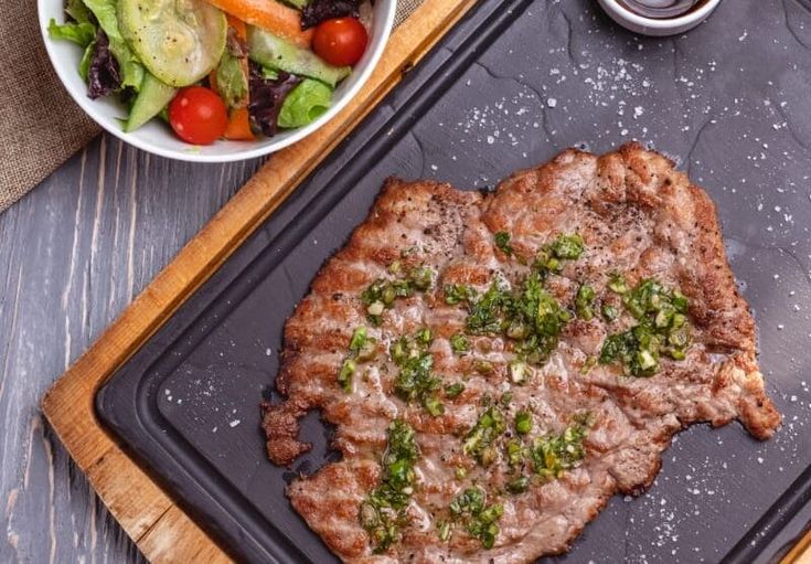 the steak is prepared and ready to be served on the grill with salad in the background