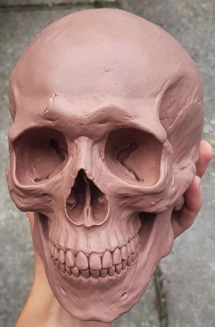 a person holding up a clay skull in front of their face and the other hand