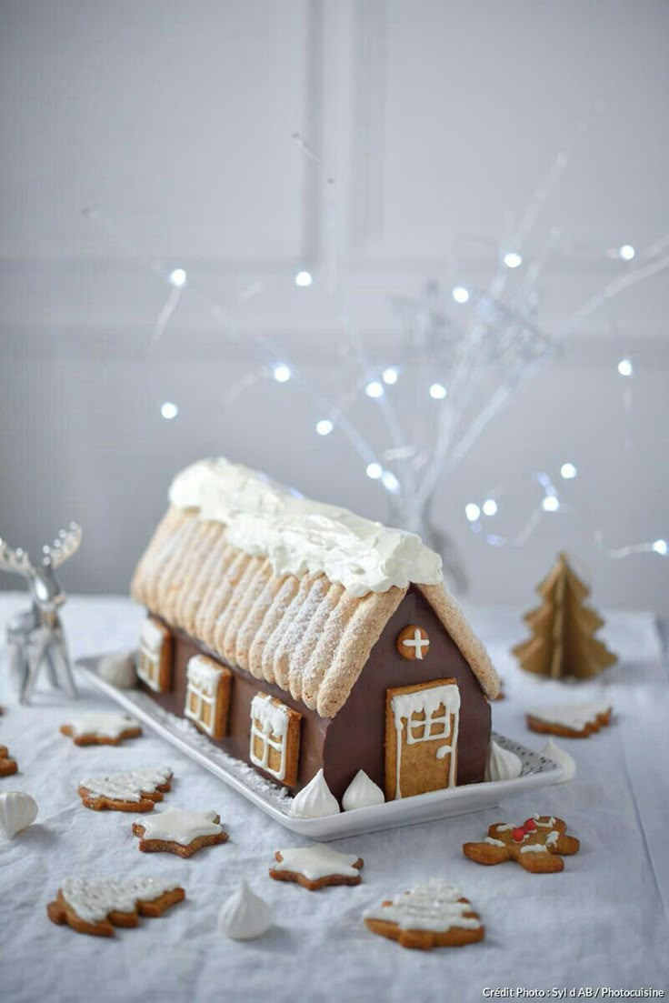 a gingerbread house with white icing and decorations on the table next to it