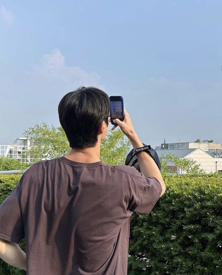 a man is taking a photo with his cell phone in front of a green hedge