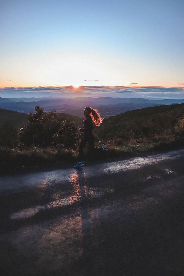 a woman standing on the side of a road at sunset