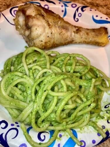 a plate with pasta, meat and green pesto sauce on it next to a piece of chicken