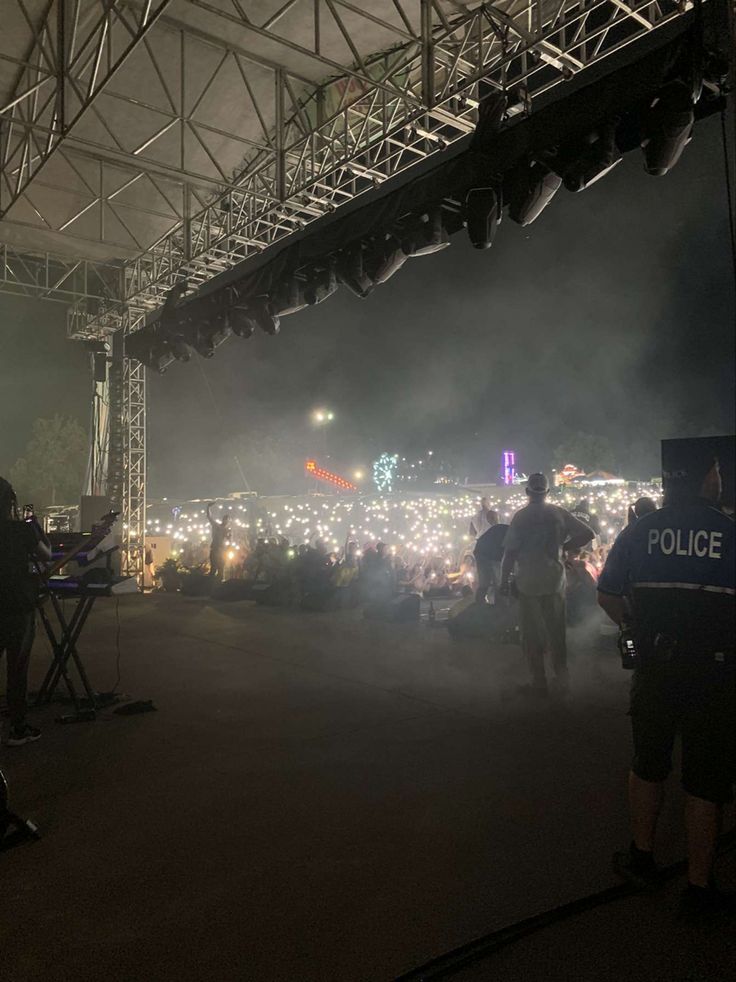 police officers standing in front of a large crowd at an outdoor music festival with lights on