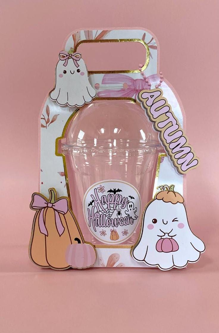 a pink bottle with an image of two ghost and pumpkins on the side, in front of a box that says happy halloween