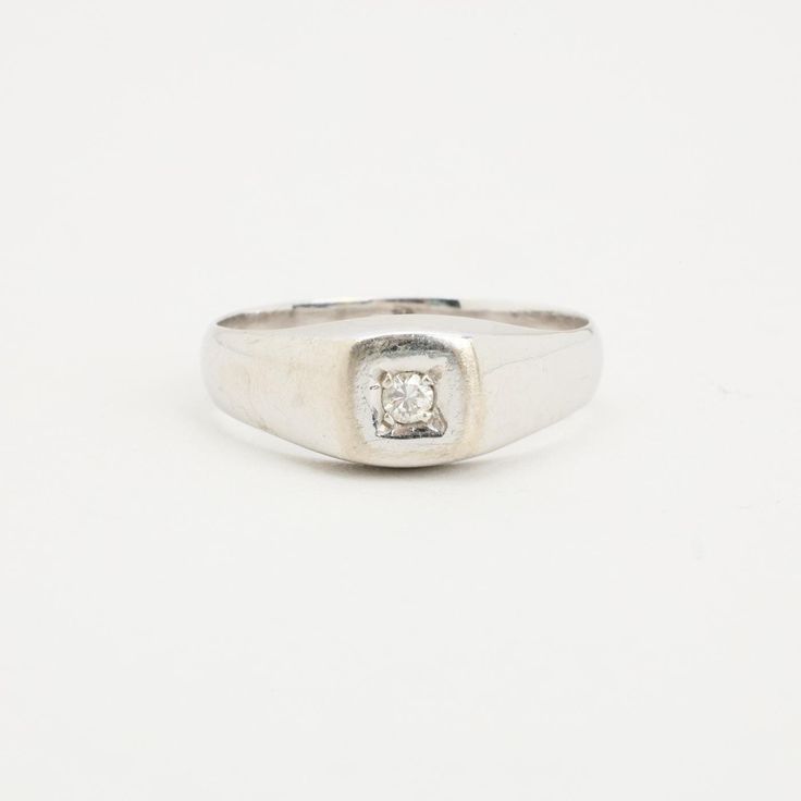 a white gold ring with a square diamond set in the center, on a plain surface