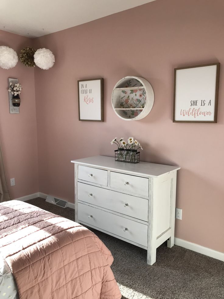 a white dresser sitting next to a bed in a room with two pictures on the wall