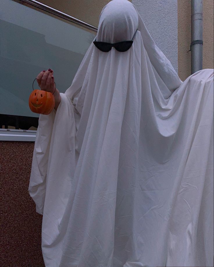 a person dressed as a ghost holding a pumpkin