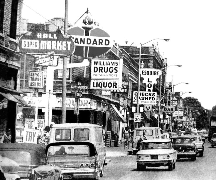 black and white photograph of cars driving down the street in an old time town area