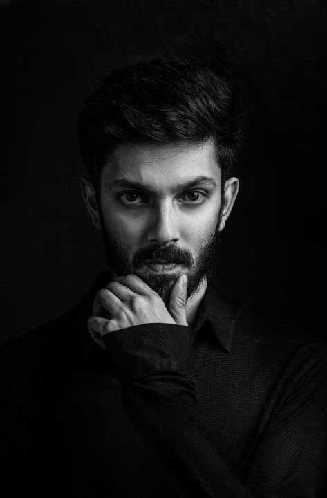 a black and white photo of a man with his hand on his chin looking at the camera