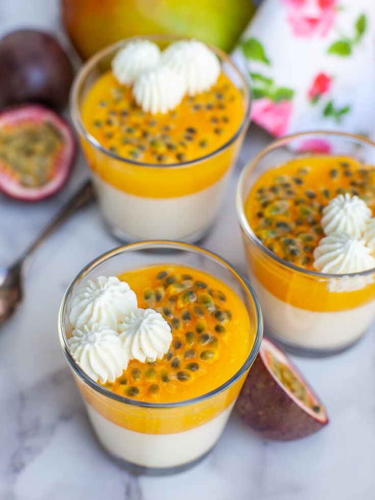 three desserts with fruit and whipped cream in small glasses on a marble countertop