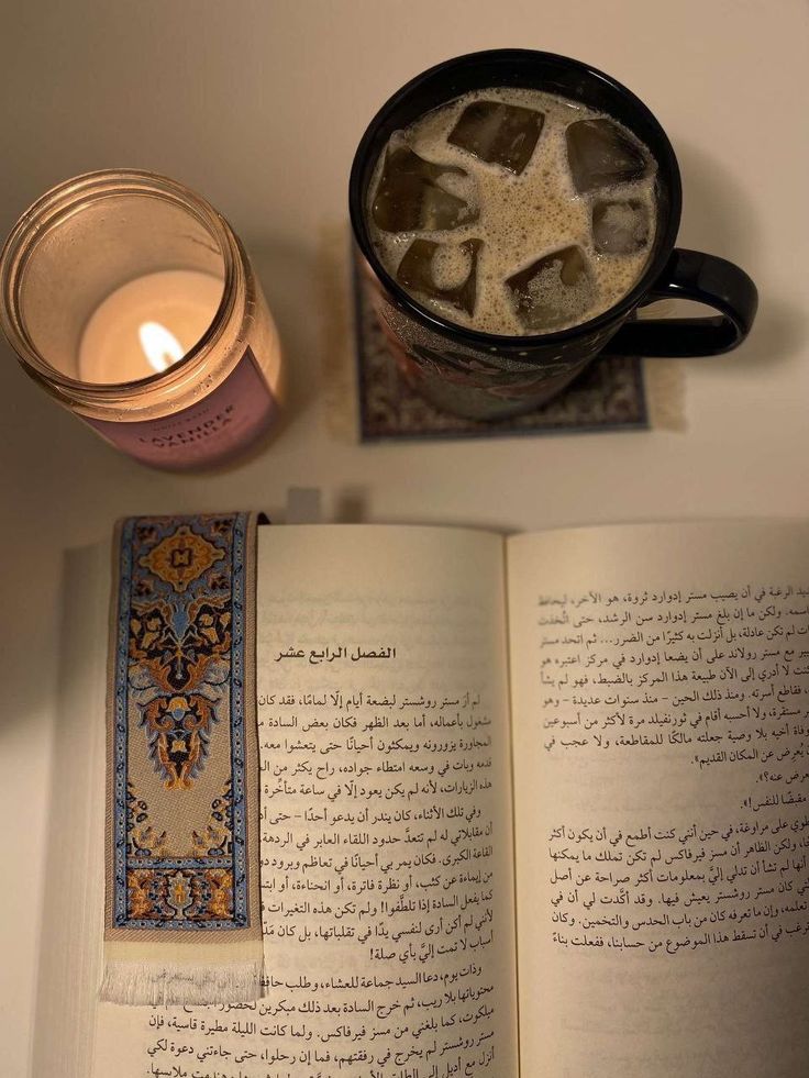 an open book with ice cubes in it next to a lit candle and cup of tea