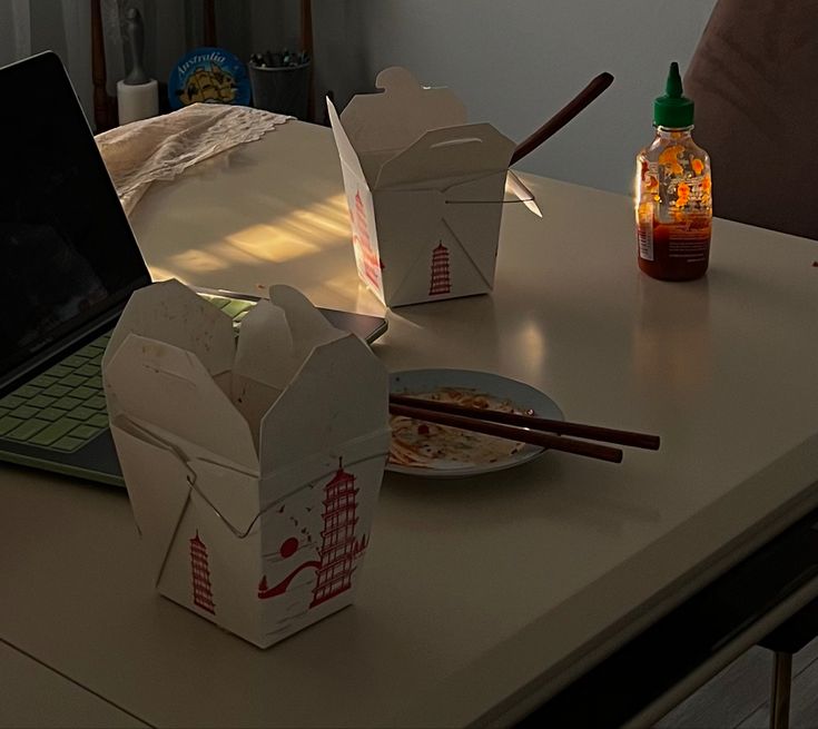 a laptop computer sitting on top of a table next to some boxes and chopsticks