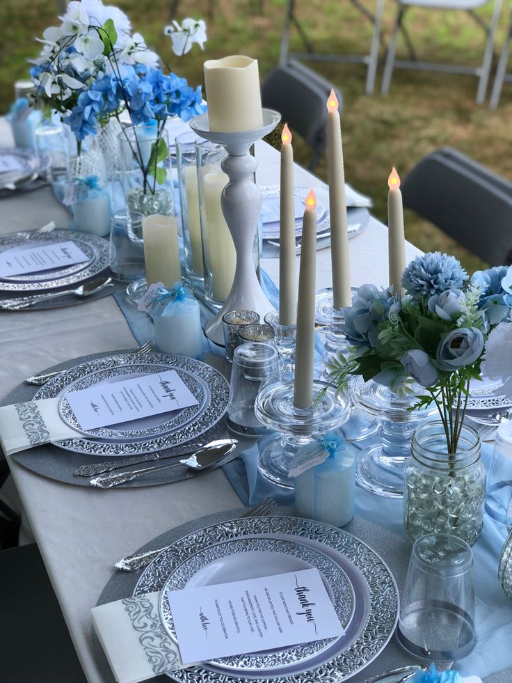 the table is set with blue and white flowers, candles, and place settings for dinner