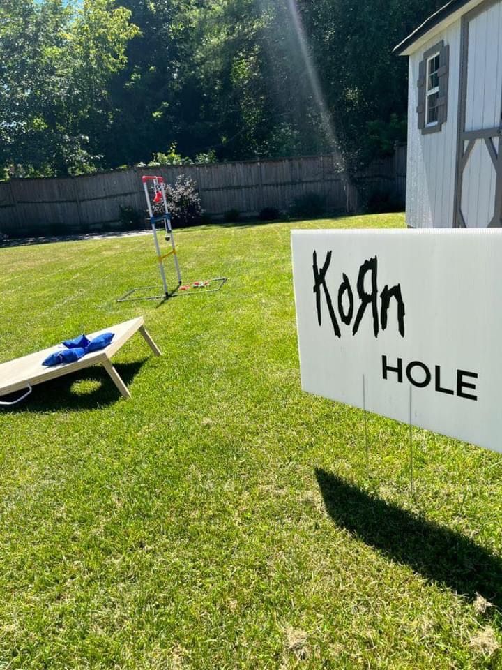 a sign that says korn hole in front of a small white shed on the grass