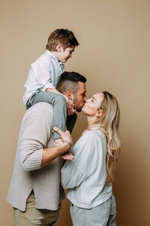 a man, woman and child kissing each other in front of a brown wall with the caption's name on it