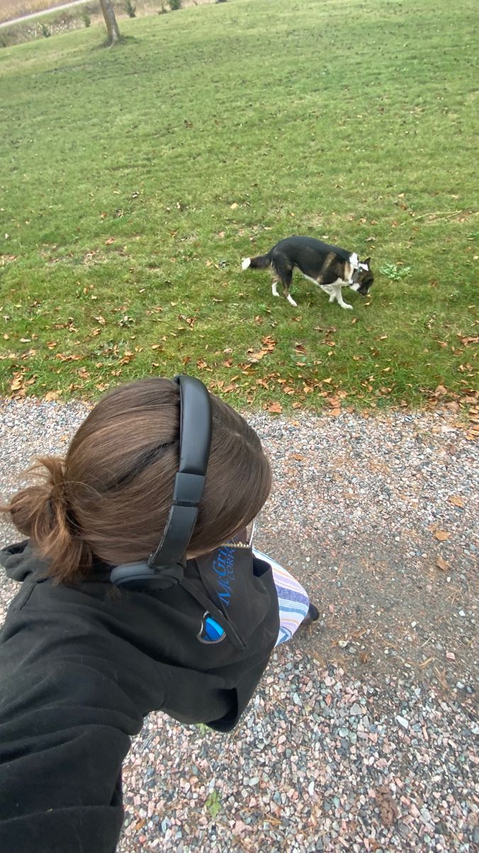 a woman is looking at a dog on the ground with her headphones in her ears