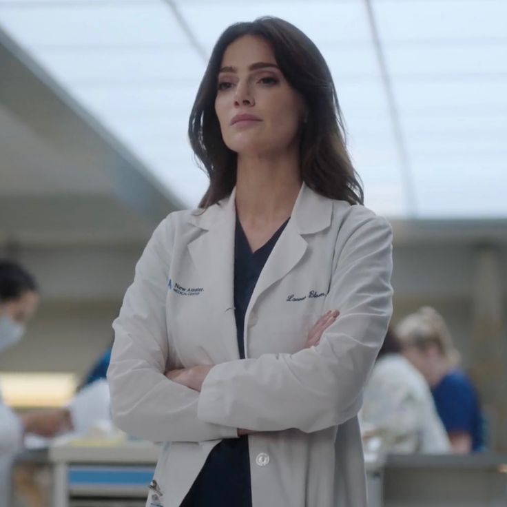 a woman in a lab coat standing with her arms crossed and looking off to the side