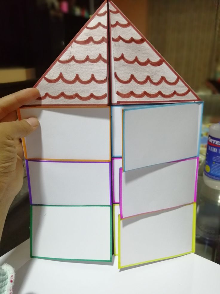 someone is holding up a small building made out of folded paper and colored construction material