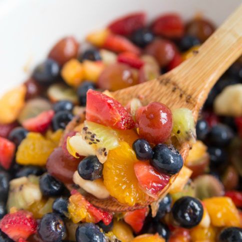 a wooden spoon full of fruit salad in a white bowl with the words honey glazed fruit salad above it