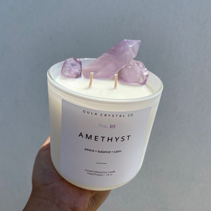 a hand holding up a candle with amethyst on it