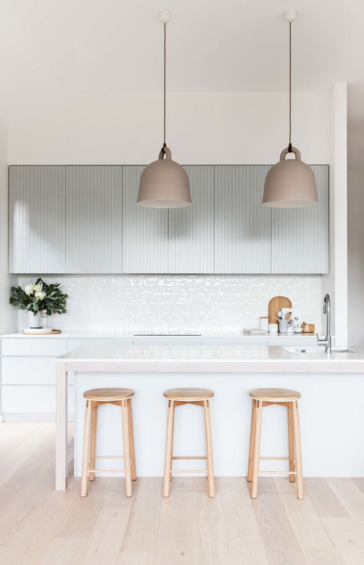 three wooden stools sit in front of a white kitchen island with two pendant lights over it