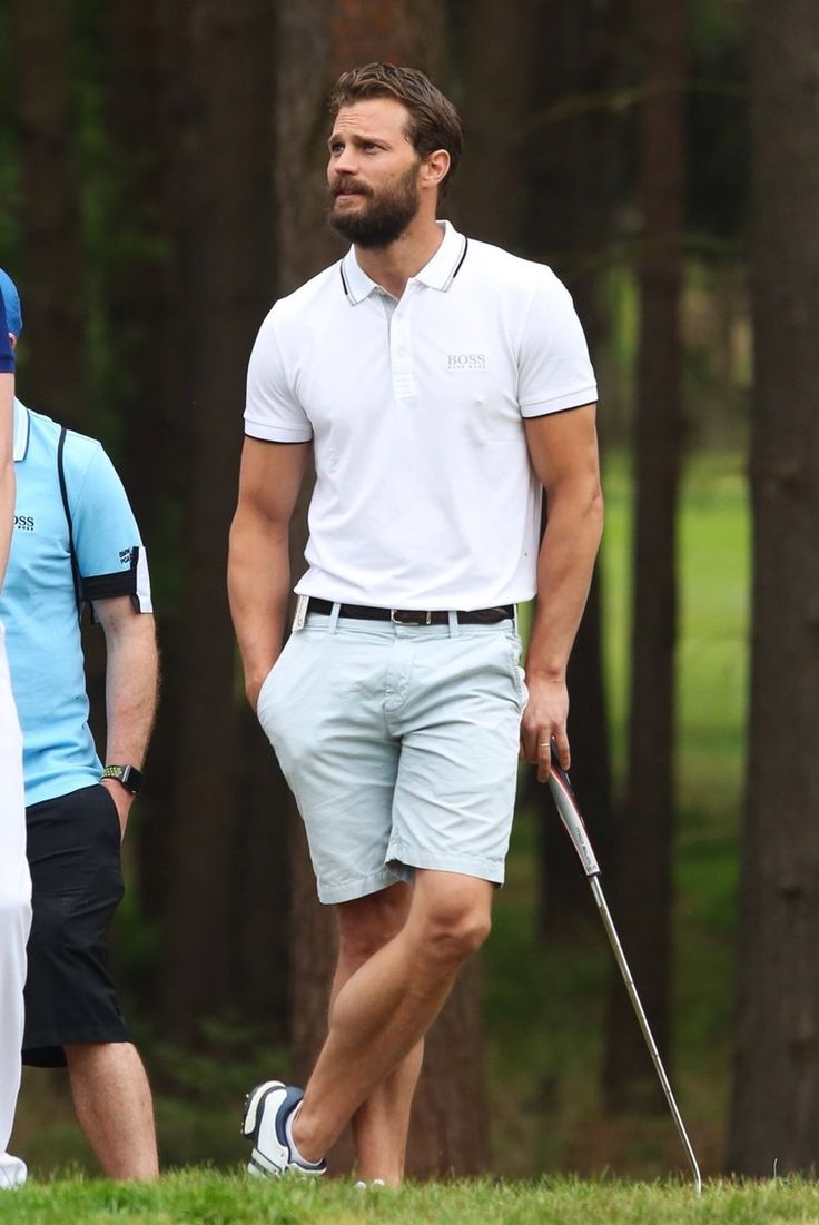 a man in white shirt and blue shorts holding a golf club while standing next to another man