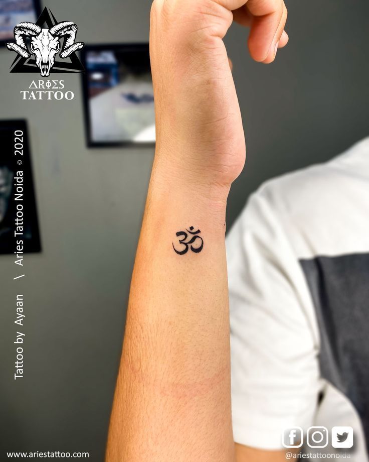 a person with a tattoo on their arm holding up a small wristband that has an om symbol on it