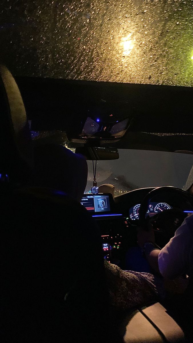 two people sitting in a car at night with the lights on and one person driving