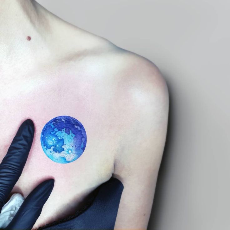 a woman's shoulder with a blue planet tattoo on her left shoulder and black gloves